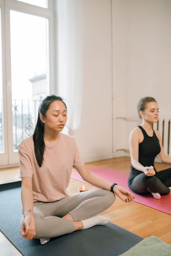 Two women meditating in lotus pose, focusing on mental health and relaxation.